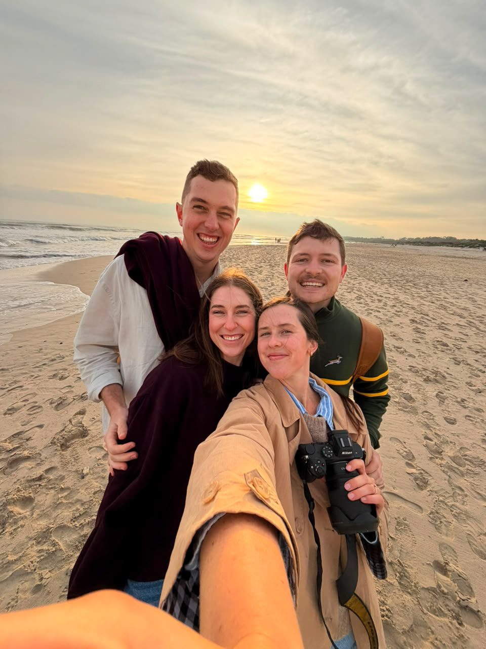 Four friends taking a selfie on the beach as the sun sets behind them — straight out of camera