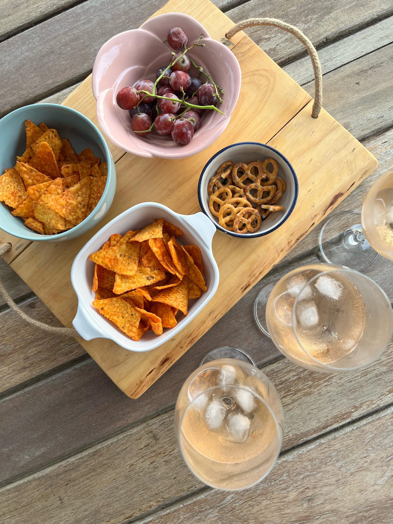 A wooden board of snacks and chilled rosé on an outdoor table, from above — straight out of camera