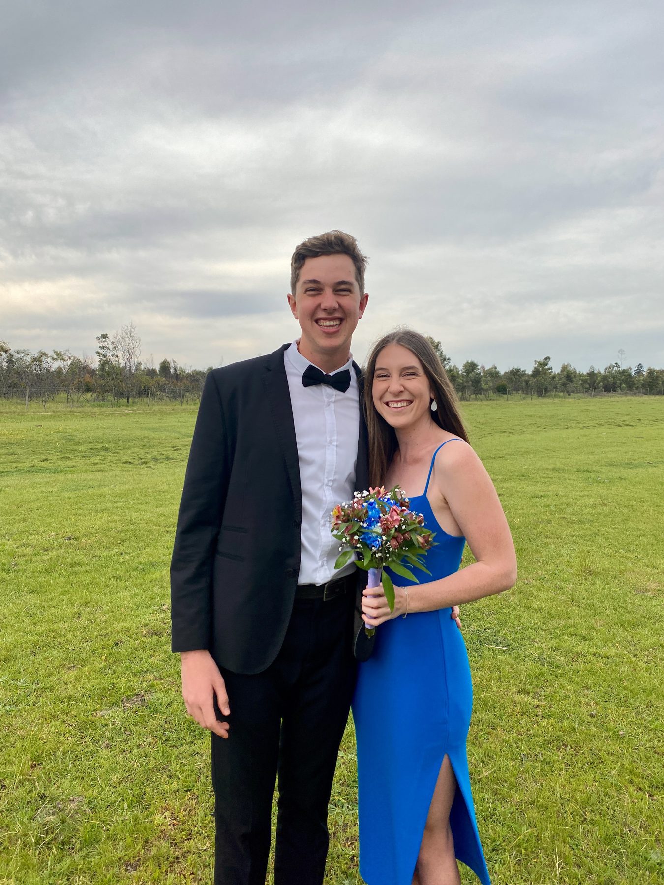 A couple in formal wear standing in a field, she in a bright blue dress with a bouquet — straight out of camera
